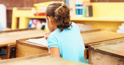 Rear view of a young school girl sitting at her desk writing her exam paper Rear view of a young school girl sitting at her desk writing her exam paper