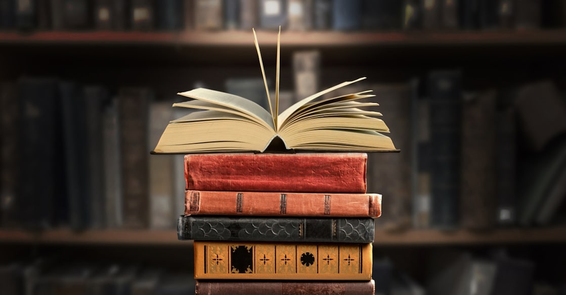 A stack of new study books on the table against the background of a bookshelf in library.