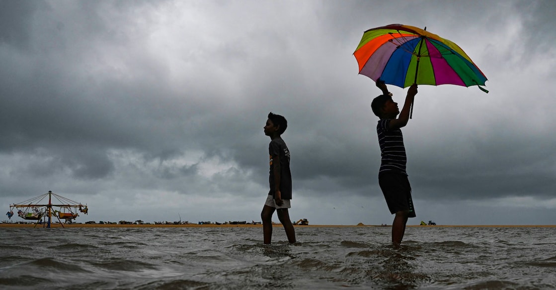 Boys walk with an umbrella amid gusty winds as dark clouds loom over the Marina beach in Chennai on November 11, 2022. (Photo by Arun SANKAR / AFP)