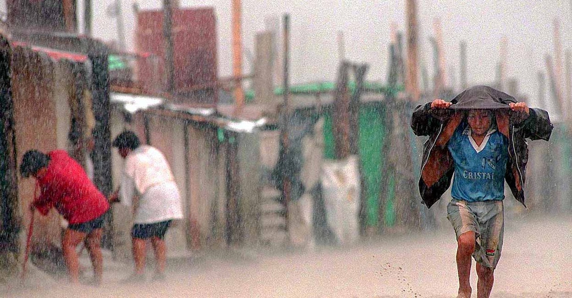 YER98-PERU-EL NINO 1 A child shields himself from torrential rains with his jacket as he runs through a flooded dirt street while local residents(L) sweep mud and water out of their shacks in the town of Tuman, 820Km north of Lima, 17 March. Health authorities report that the flooding caused by the meteorological phenomenon "El Nino" has exacerbated poor sanitary conditions in the poorest parts of Peru, provoking outbreaks of cholera, malaria, dysentery and conjunctivitis. (Photo by JAIME RAZURI / AFP)