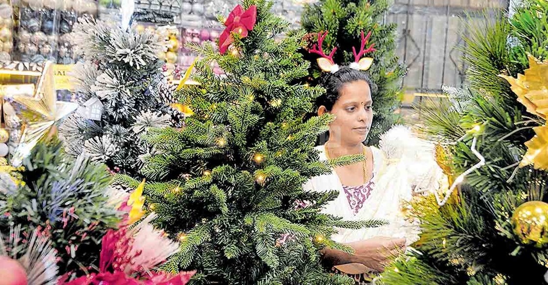 1xmas ക്രിസ്മസ് ആഘോഷത്തിനായി നക്ഷത്രങ്ങളും ട്രീകളും അടക്കമുള്ളവ വിൽക്കാൻ നഗരത്തിൽ പ്രത്യേകമായി സജ്ജീകരിച്ച കടയിൽ, വിവിധ ഉൽപന്നങ്ങൾ പരിശോധിക്കുന്ന സ്ത്രീ.