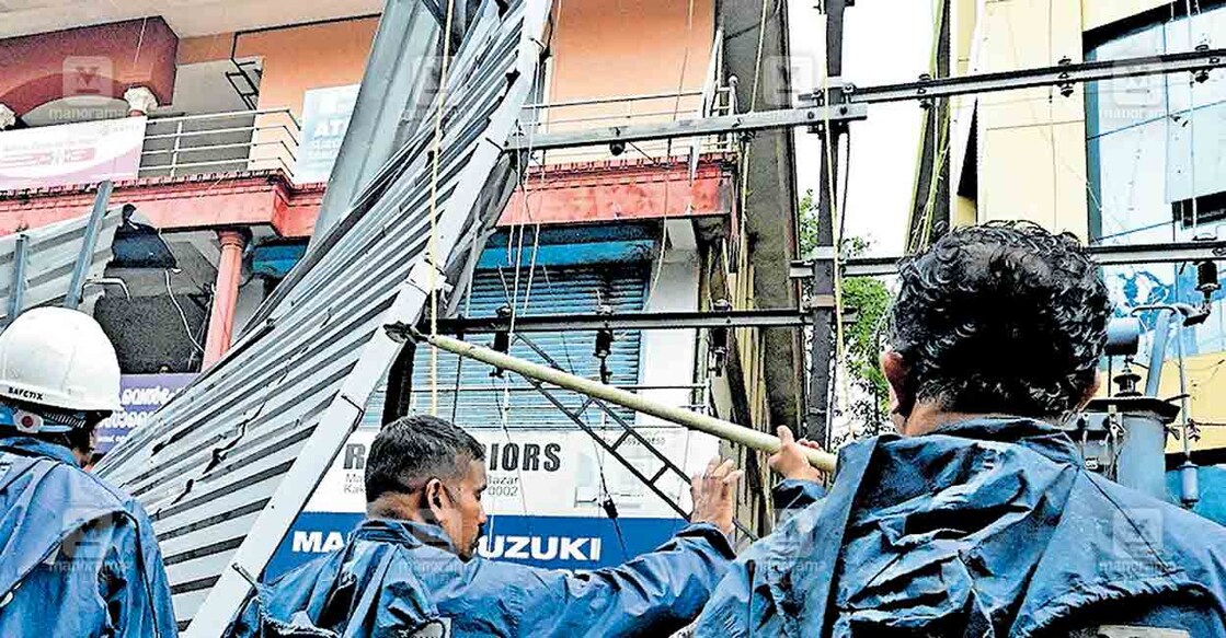 കഴിഞ്ഞ ദിവസത്തെ കാറ്റിൽ കണ്ണൂർ തെക്കി ബസാറിൽ വൈദ്യുതി ലൈനിലേക്ക് വീണ റൂഫിങ് ഷീറ്റിന്റെ ഭാഗങ്ങൾ താഴെ ഇറക്കാനുള്ള കെഎസ്ഇബി ജീവനക്കാരുടെ ശ്രമം.  ചിത്രം: മനോരമ  