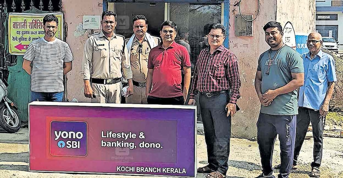 kottayam-madhyapradesh-fake-bank മധ്യപ്രദേശിൽ കണ്ടെത്തിയ വ്യാജ ബാങ്കിൽ പൊലീസും ഉദ്യോഗസ്ഥരും പരിശോധന നടത്തിയപ്പോൾ. പിന്നിൽ കാണുന്ന കെട്ടിടത്തിലാണു വ്യാജ ബാങ്ക് പ്രവർത്തിച്ചിരുന്നത്. ബാങ്കിന്റെ ബോർഡാണ് ഇളക്കി താഴെവച്ചിരിക്കുന്നത്.