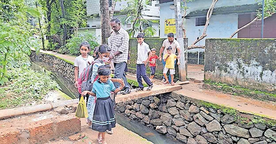 തിരൂരങ്ങാടി പുളിഞ്ഞിലംപാടം അങ്കണവാടിക്കു മുൻപിലെ തോടിനു മുകളിൽ വൈദ്യുതപോസ്റ്റിട്ട് ഒരുക്കിയ നടപ്പാലത്തിലൂടെ നടന്നുപോകുന്ന കുട്ടികളും രക്ഷിതാക്കളും.  