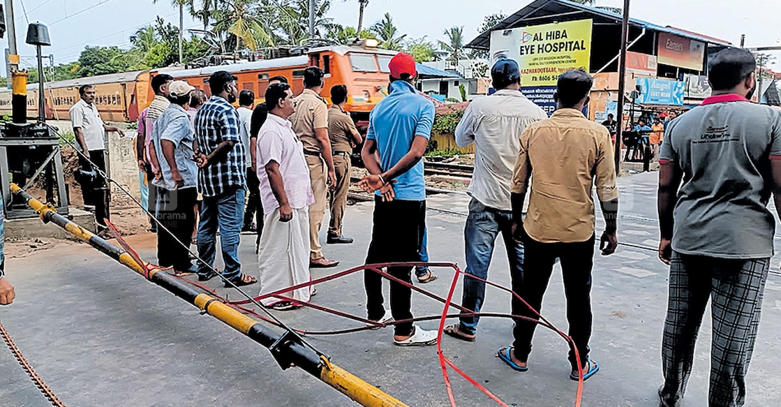 തുമ്പ സ്റ്റേഷൻകടവിൽ തകർന്നു വീണ റെയിൽവേ ഗേറ്റ്. പ്രതിഷേധിക്കുന്ന നാട്ടുകാരെയും കാണാം.