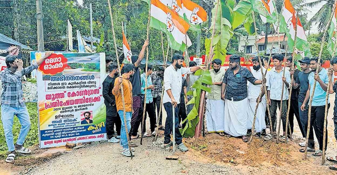 thiruvananthapuram-youth-congress-protest-road-collapsed കാരേറ്റ് - പാലോട് റോഡിന്റെ യാത്രാദുരിതവും നിർമാണ അഴിമതിയും അന്വേഷിക്കണം എന്നാവശ്യപ്പെട്ട് യൂത്ത് കോൺഗ്രസ് പാങ്ങോട് മണ്ഡലം കമ്മിറ്റി സംഘടിപ്പിച്ച പ്രതിഷേധ സമരം യൂത്ത് കോൺഗ്രസ് സംസ്ഥാന സെക്രട്ടറി അമി തിലക് റോഡിലെ കുഴിയിൽ വാഴ നട്ട് ഉദ്ഘാടനം ചെയ്യുന്നു.