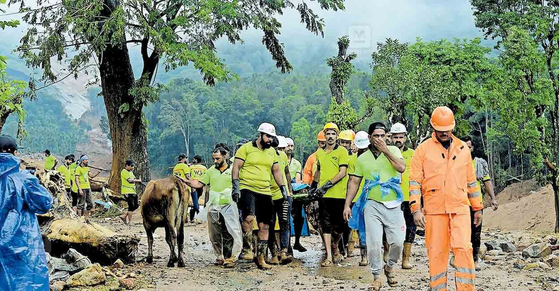 wayanad-rescue-workers-moving-towards-an-ambulance-with-a-dead-body മുണ്ടക്കൈയിൽ ഉരുൾപൊട്ടലിൽ തകർന്ന വീട്ടിനുള്ളിൽ നിന്നു കണ്ടെത്തിയ മൃതദേഹവുമായി ആംബുലൻസിനടുത്തേക്ക് നീങ്ങുന്ന രക്ഷാപ്രവർത്തകർ.