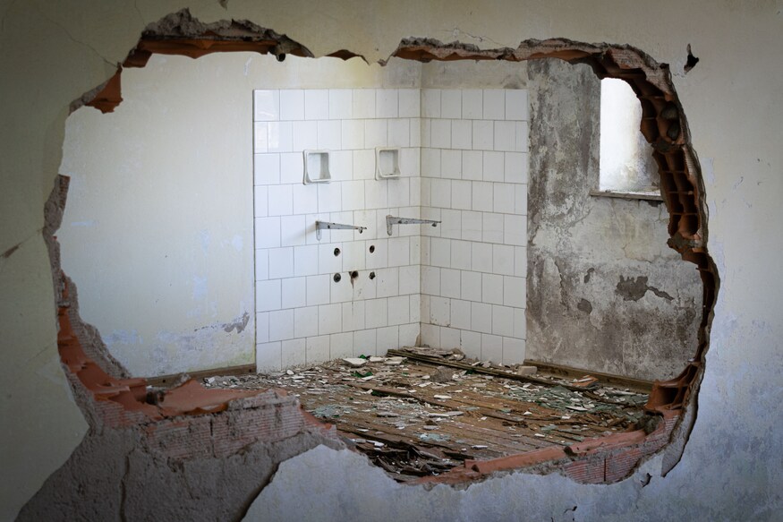 Destroyed wall that opens onto the remains of a bathroom, white tiles and rubble