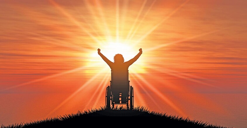 3D silhouette of a female in a wheelchair with her arms raised against a sunset ocean