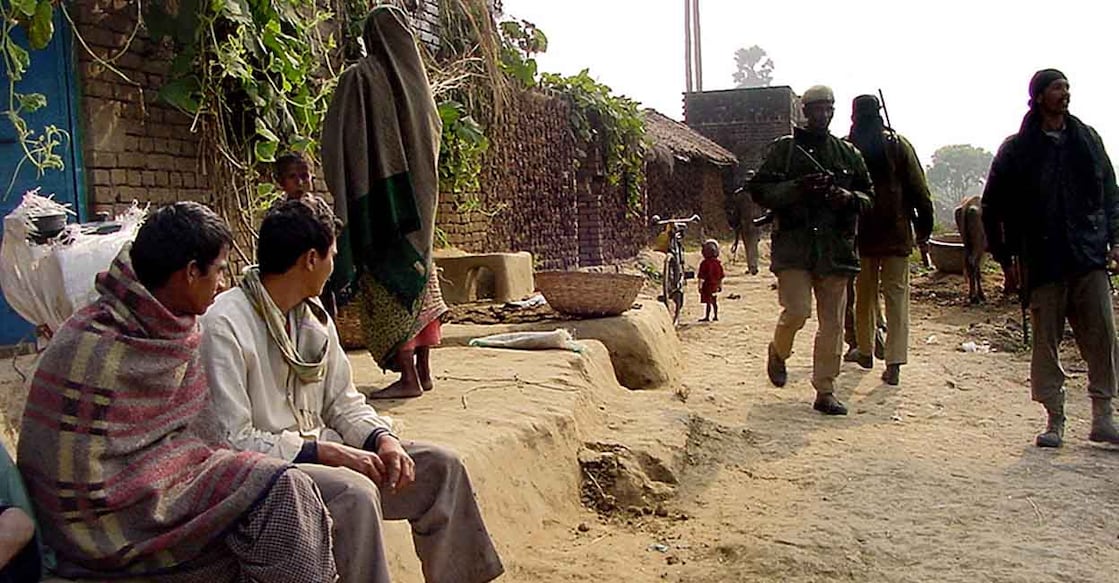 Two men (L) look at Indian commandos (R) as they patrol a street in Barichak village near Masaurhi town , 26 December 2002 some 40 kilometers (25 miles) from the state capital Patna where left-wing rebels killed seven people overnight. The rebel, who had called for a ban on harvesting until the extortion was paid, killed low-caste farmers. AFP PHOTO (Photo by AFP)