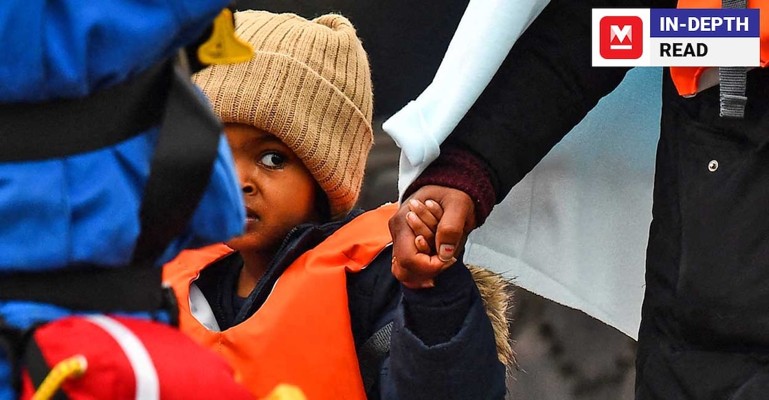 BRITAIN-EU-FRANCE-POLITICS-MIGRATION A migrant child reacts while holding the hand of a migrant adult as UK coastguards help them to disembark from the UK Border Force vessel Vigilant, after they were picked up at sea while attempting to cross the English Channel, and brought to the Marina in Dover, southeast England, on March 16, 2022. - The high number of migrants crossing to Britain from mainland Europe has become a political headache for British government. (Photo by Ben STANSALL / AFP)