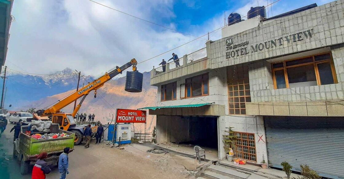 Joshimath | (PTI Photo) അപകടാവസ്ഥയിലായ ഹോട്ടൽ പൊളിച്ചുകളയുന്നതിനു മുൻപ് മുകളിൽനിന്ന് വെള്ളത്തിന്റെ ടാങ്കുകൾ നീക്കുന്നു. (PTI Photo)