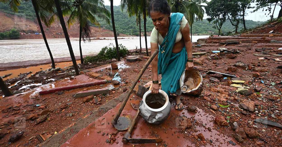 അങ്കോല ഷിരൂരിൽ കുന്ന് ഇടിഞ്ഞ് ഗംഗാവലി നദിയിലേക്ക് വീണപ്പോൾ മറുഭാഗത്തേക്ക് സുനാമി പോലെ വെള്ളം മുകളിലേക്ക് ഇരച്ചു കയറി തകർന്നാതാണ് സന്നിയുടെ വീട്. സംഭവസമയത്ത് വീടിനുള്ളിൽ ഭക്ഷണം പാകം ചെയ്തു കൊണ്ടിരുന്ന സന്നി ഒഴുക്കിൽ പെട്ടു. ഇത് വരെയും സന്നിയെ കണ്ടെത്താനായിട്ടില്ല. 6ൽ കൂടുതൽ വീടുകളാണ് വെള്ളം ഇരച്ചു കയറി തകർന്നത്.  രണ്ടിൽ കൂടുതൽ വീടുകൾക്ക് തറ മാത്രമാണ് ബാക്കി. മണ്ണിടിഞ്ഞ കരയും മറുകരയായ മാടങ്കേരി ഉൾവരെ പ്രദേശവും തമ്മിൽ ഏകദേശം അഞ്ഞൂറ് മീറ്ററിലധികം ദൂരമുണ്ട്.  മാടങ്കേരി ഉൾവരെയിൽ സന്നിയുടെ തകർന്ന വീടിനരികെ എത്തിയതാണ് സഹോദരി സന്നി ഭീരഗൗഡ. ചിത്രം: അഭിജിത്ത് രവി ∙മനോരമ