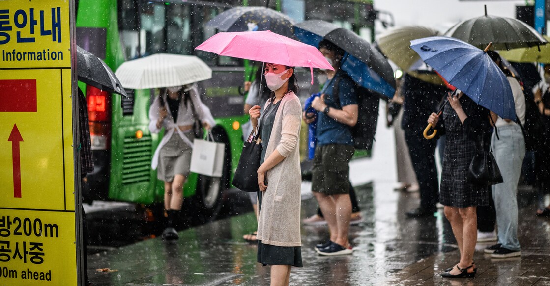 Pedestrians use umbrellas to shelter from a heavy downpour as they wait for a bus in Seoul on June 23, 2022. (Photo by Anthony WALLACE / AFP)