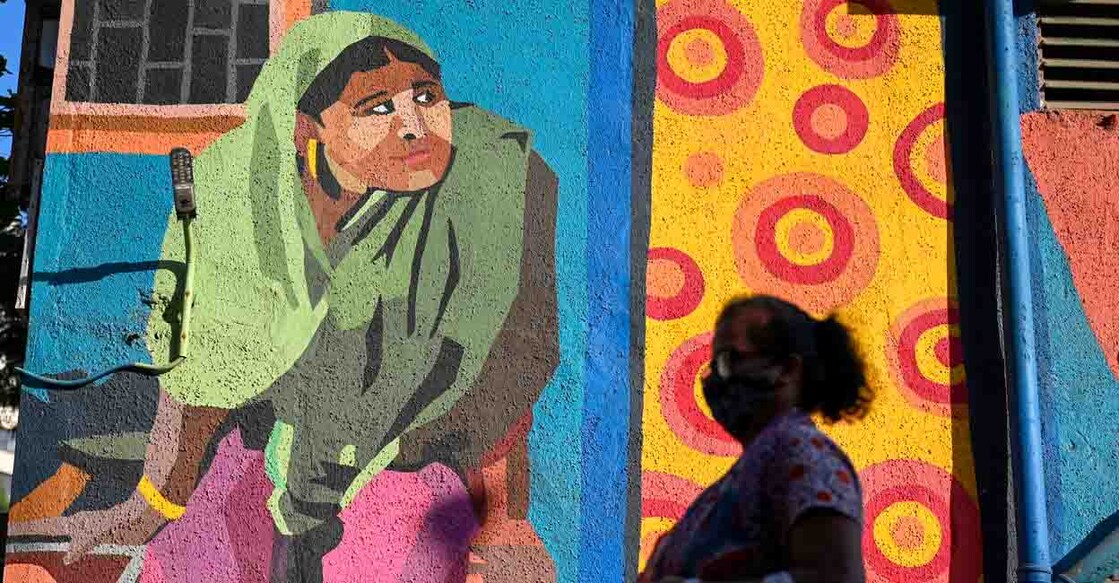 A woman walks past a mural portraying daily life in the Dharavi slums in Mumbai on February 22, 2022. (Photo by Punit PARANJPE / AFP)