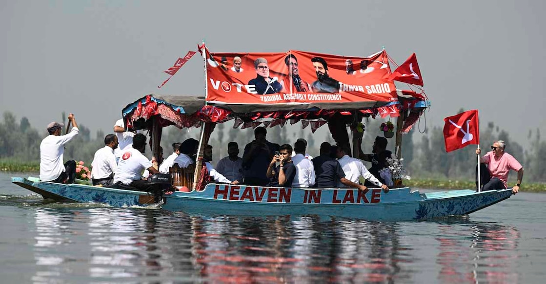 Omar Abdullah (R), the leader of Jammu and Kashmir National Conference (JKNC), holding his party's flag rides a boat in Dal Lake during an election campaign rally in Srinagar on September 22, 2024, ahead of the second phase of voting during assembly election. (Photo by TAUSEEF MUSTAFA / AFP)