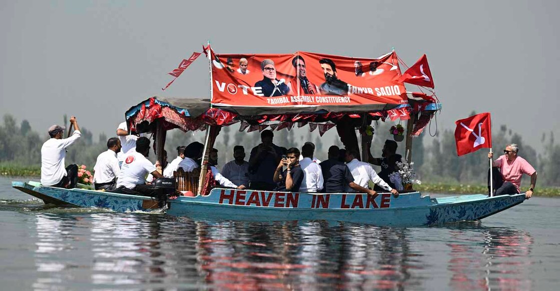 INDIA-KASHMIR-POLITICS-VOTE Omar Abdullah (R), the leader of Jammu and Kashmir National Conference (JKNC), holding his party's flag rides a boat in Dal Lake during an election campaign rally in Srinagar on September 22, 2024, ahead of the second phase of voting during assembly election. (Photo by TAUSEEF MUSTAFA / AFP)