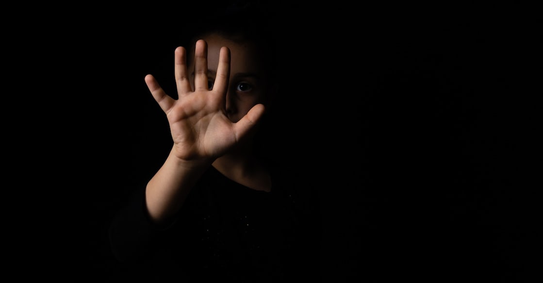 little girl with a raised hand making a stop sign gesture on a black background. harassment and child abuse prevention concept.