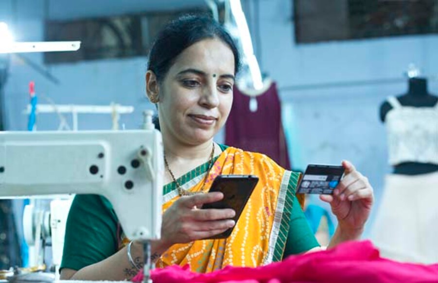 Working woman using mobile phone and credit card at textile factory