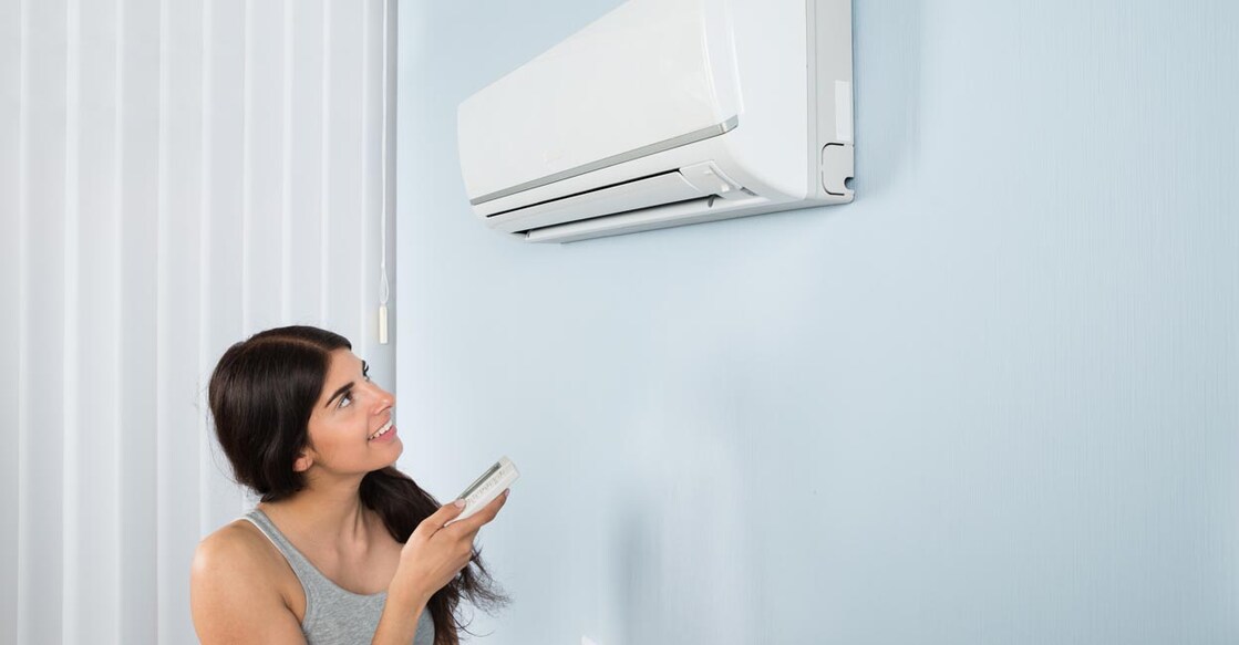 Young Happy Woman Holding Remote Control Air Conditioner In House