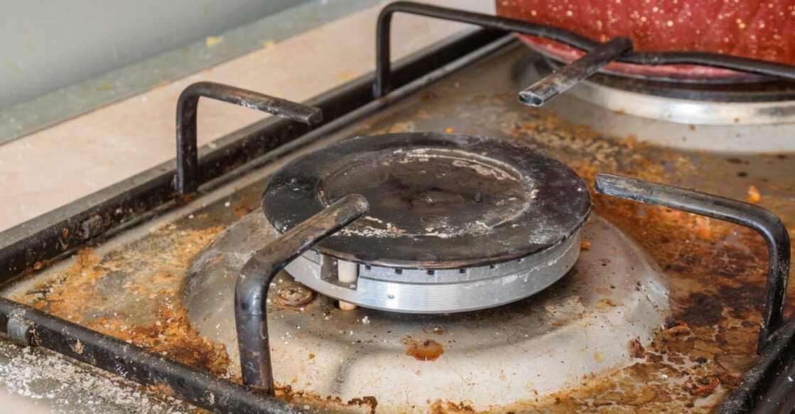 Dirty gas stove surface. One gas burner and a cast-iron grate of a gas stove, surrounded by leftover food and drinks with spilled salt. Selective focus.