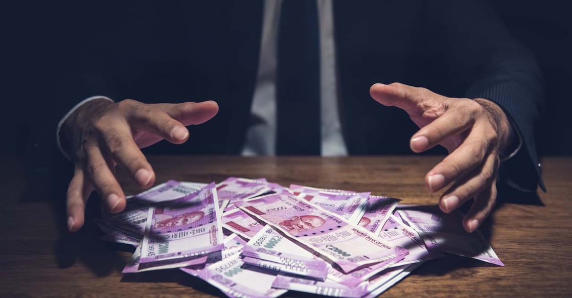 876037514 Businessman taking pile of money, Indian Rupee banknotes, on his desk in a dark office - corruption concept