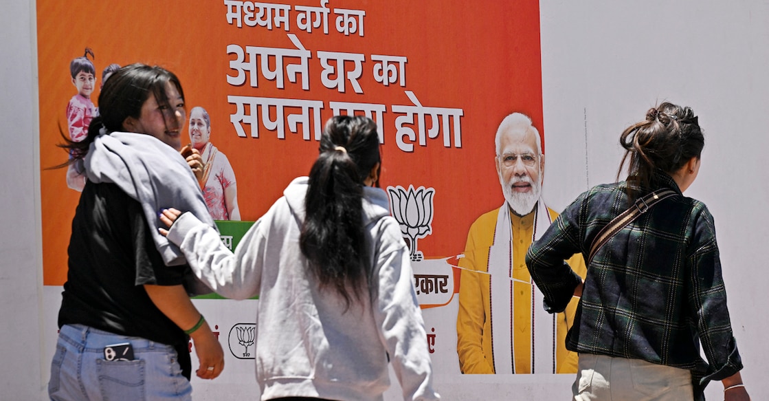 This photograph taken on May 17, 2024 shows women walking past a campaign poster of the ruling Bharatiya Janata Party (BJP) picturing their leader and India's Prime Minister Narendra Modi outside the party office in Leh, summer capital of the country's union territory of Ladakh, during the nation's ongoing general election. - Buddhist monks and Muslims in the Indian Himalayan territory of Ladakh turned out to vote on May 20, demanding statehood and that their local culture be protected in the overwhelmingly Hindu nation. (Photo by Tauseef MUSTAFA / AFP)