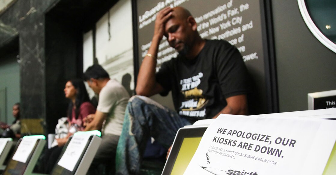 A man waits for his flight next to a printed sign displayed on a kiosk of Spirit Airlines after a global outage at LaGuardia Airport in the Queens borough of New York, on July 19, 2024. - Airlines, banks, TV channels and other businesses were disrupted worldwide on Friday following a major computer systems outage linked to an update on an antivirus program. (Photo by Leonardo Munoz / AFP)