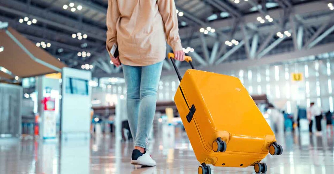 Young female traveler passenger walking with a yellow suitcase at the modern Airport Terminal, Back view of woman on her way to flight boarding gate, Ready for travel or vacation journey
