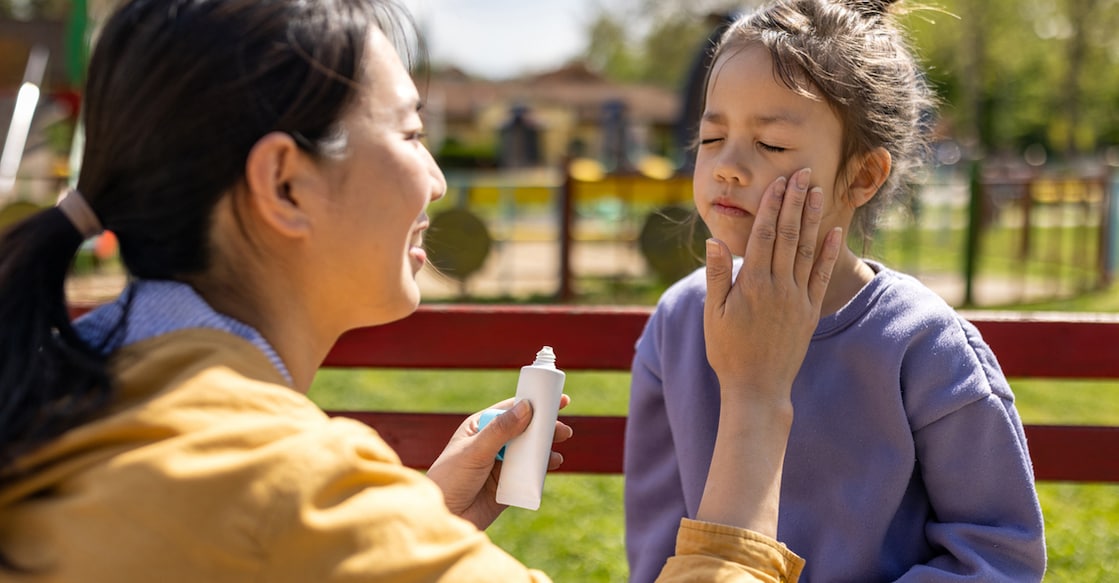 Mid adult Japanese woman applying sun-screen to her daughters face