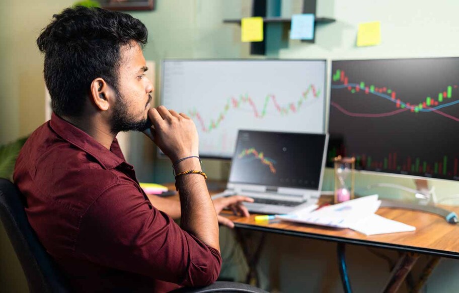 Side view of Trader analyzing share market by looking charts in multiple monitors or making strategy at home office - concept of studying equity market, waiting for success.