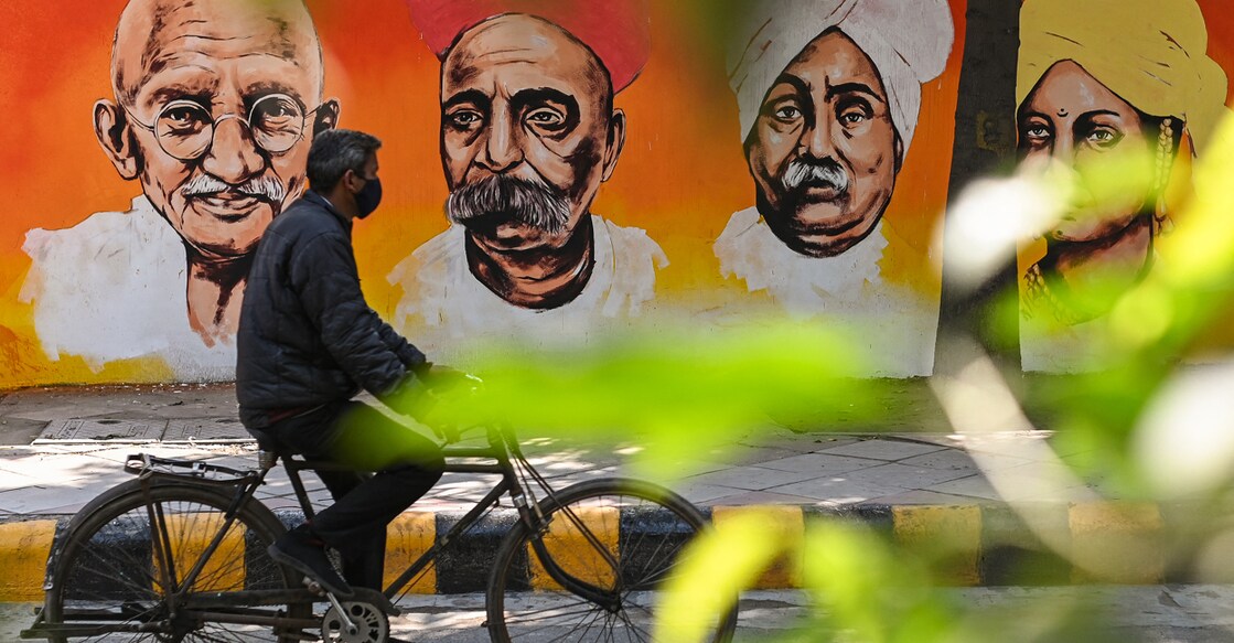 A cyclist peddles past a wall mural depicting prominent figures of the Indian freedom struggle in New Delhi on February 13, 2022. (Photo by Sajjad HUSSAIN / AFP)