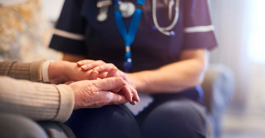 1129903329 A female nurse consoles a senior patient at home