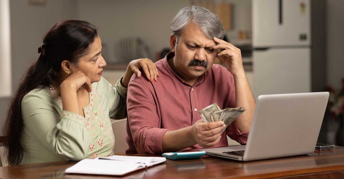 Worried mature couple counting money at white using laptop indoors