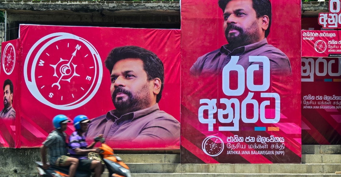 SRI LANKA-VOTE-DISSANAYAKE Motorists rides past posters of National People's Power (NPP) presidential candidate Anura Kumara Dissanayake, ahead of the country's presidential elections in Colombo on August 25, 2024. Sri Lanka's presidential hopeful Dissanayake wants a peaceful revolution after his Marxist party failed to seize power in two uprisings that left over 80,000 dead. (Photo by Ishara S. KODIKARA / AFP)