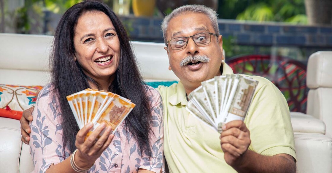 Happy mature senior Indian couple holding money rupee notes in hand while sitting at home. Savings and banking concept