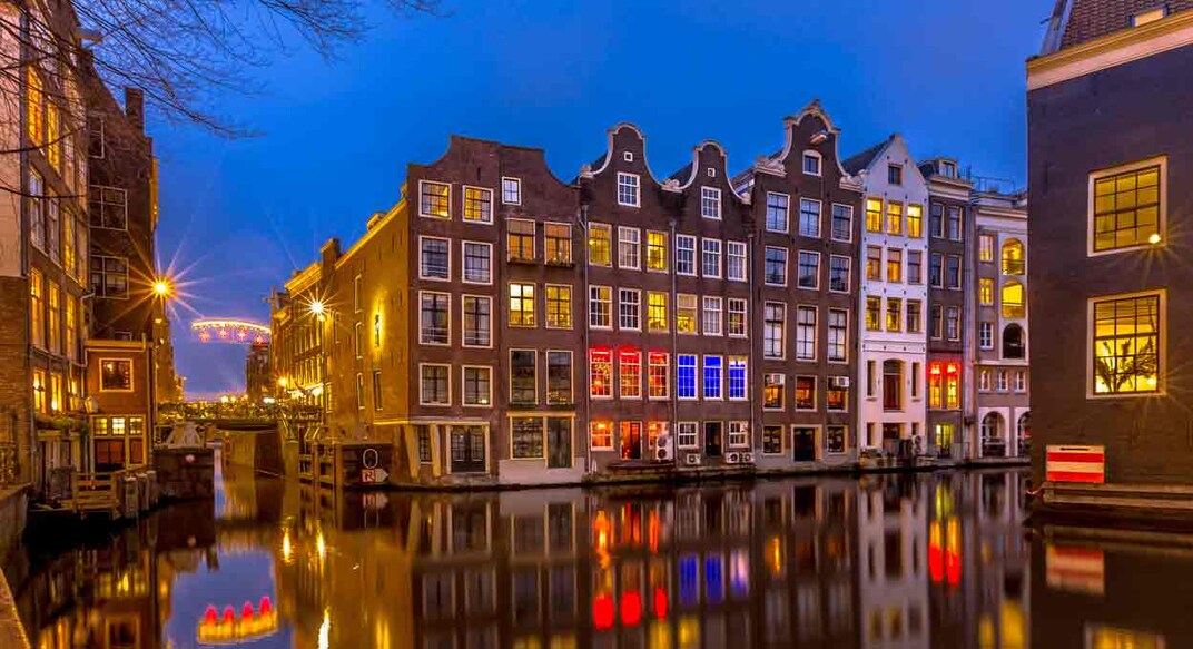 Traditional colorful canal houses at night seen from the Sint Olofsteeg on the Oudezijds Voorburgwal in the UNESCO World Heritage site of Amsterdam. Image Credit : CreativeNature_nl /istockphotos.com